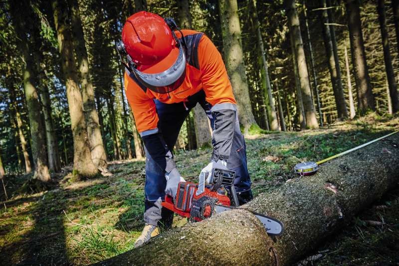 Человек использует аккумуляторную пилу Einhell GP-LC 36/35 Li-Solo при распиле поваленного дерева, видны опилки.